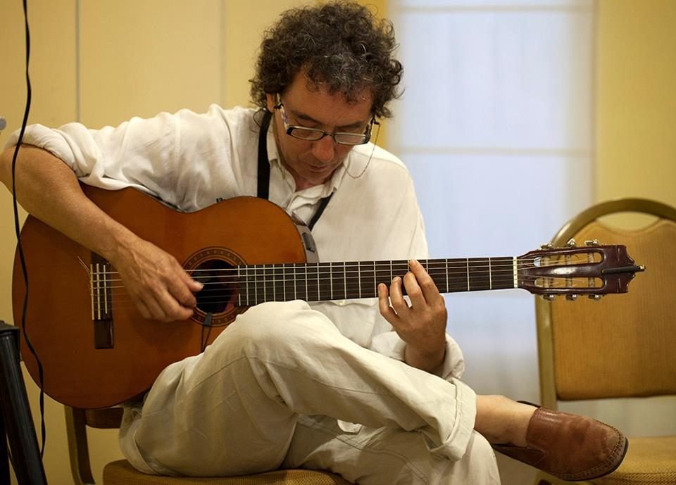 Miguel Anda concentrado tocando la guitarra, vestido de blanco